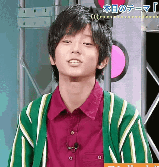 a young man wearing a green and white striped jacket and a red shirt
