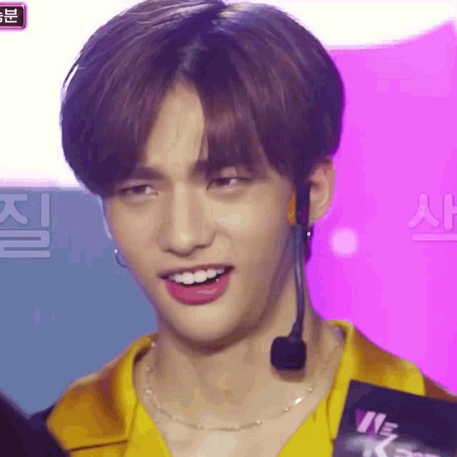 a close up of a young man wearing a yellow shirt and a microphone .