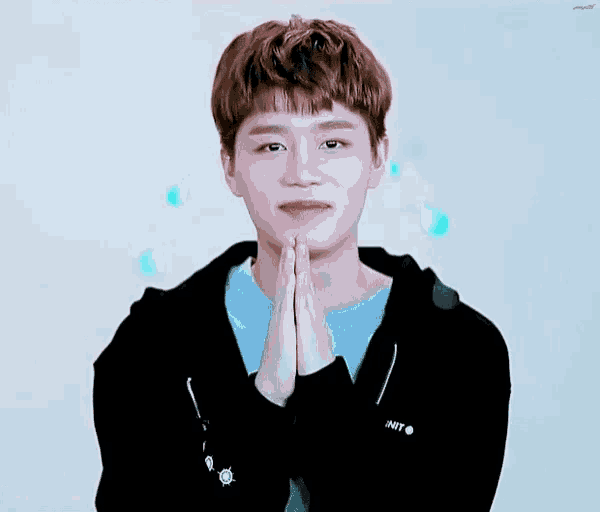 a young man wearing a blue shirt and a black hoodie is praying with his hands together