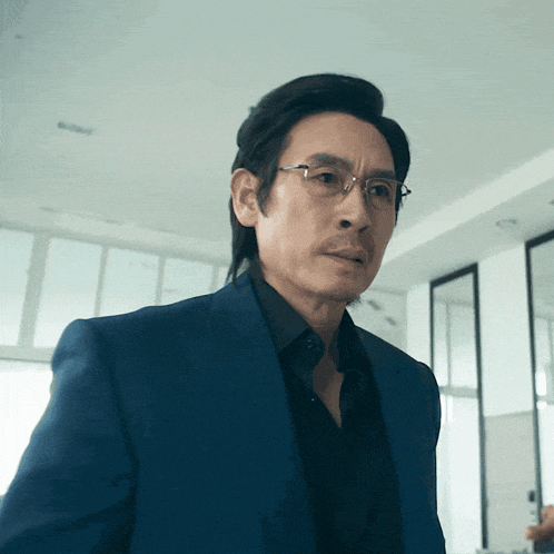 a man wearing glasses and a blue suit is looking at the camera
