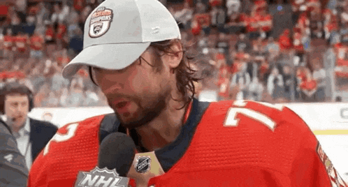 a hockey player is talking into a microphone while wearing a white hat .