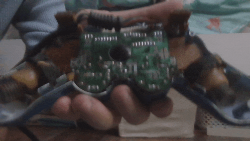 a person is holding a broken video game controller with a green board