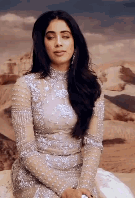 a woman in a dress with pearls on it sits on a sand dune with her eyes closed