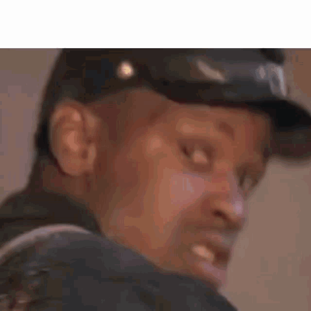 a close up of a man wearing a hat and looking at the camera .