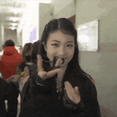 a woman wearing a black jacket and black gloves is making a heart shape with her hands