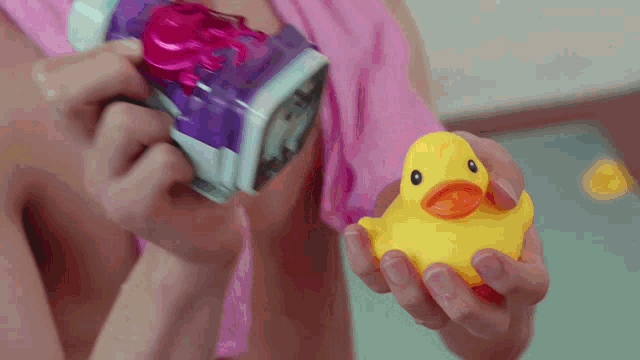 a person is holding a yellow rubber duck and a pink toy