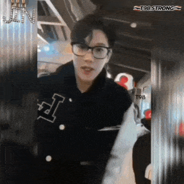 a young man wearing glasses and a black jacket with the letter i on it