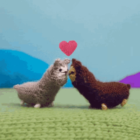 two crocheted llamas are standing next to each other with a heart flying in the air between them .