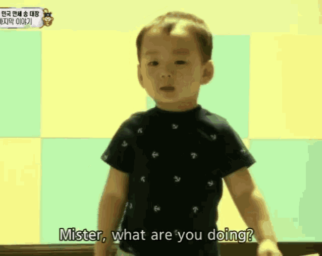 a little boy in a black shirt is standing in front of a yellow wall and says mister what are you doing .