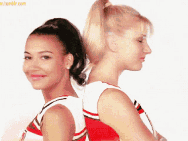two cheerleaders are standing back to back with their backs to the camera