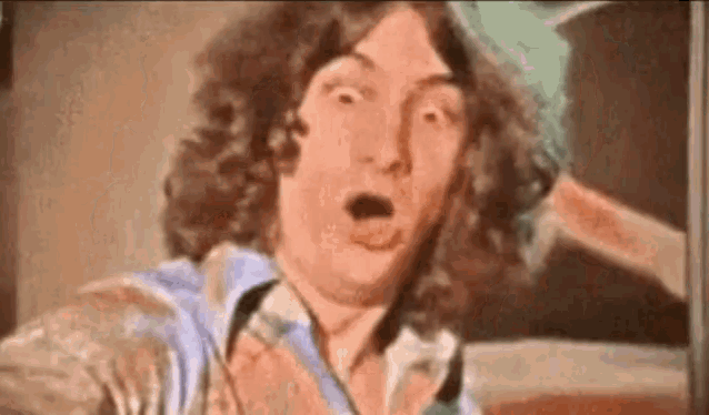 a man with long curly hair is making a surprised face in front of a painting .