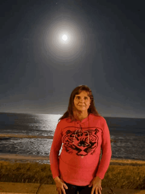 a woman in a red sweater with a tiger on it stands in front of the ocean
