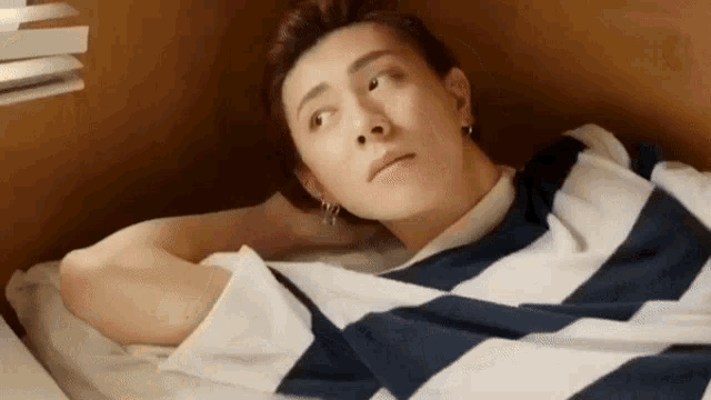 a man in a striped shirt is laying on a bed with his head on his arm .