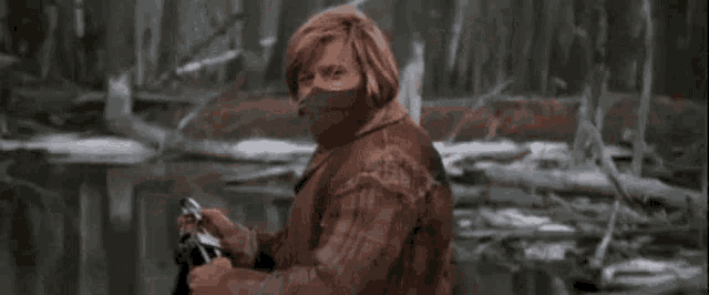 a man with a mask on his face is standing next to a river holding a fishing rod .