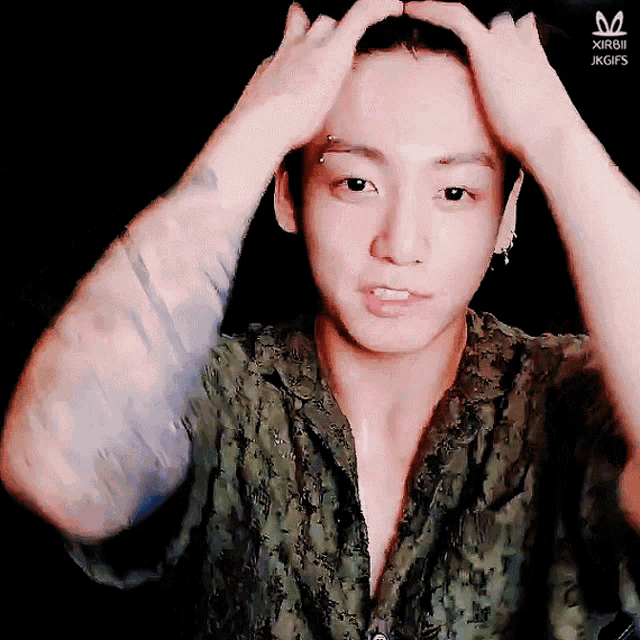 a man with a tattoo on his arm holds his hands to his head and looks at the camera