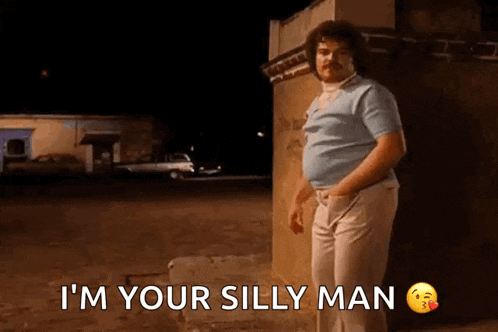 a man with a mustache is standing next to a building and says i 'm your silly man .