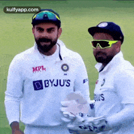 two cricket players are standing next to each other on a field and smiling .