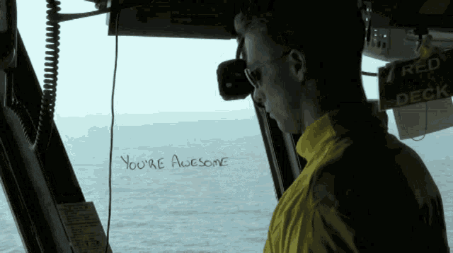 a man in a yellow shirt is looking out a window with the words " you 're awesome " written on it