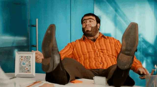 a man with a beard is sitting at a desk with his feet up