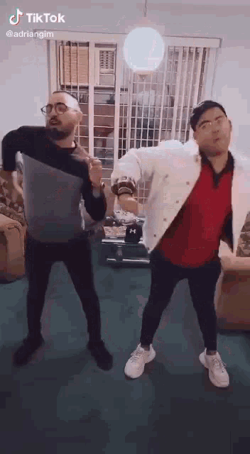two men are dancing together in a living room in a tiktok video .