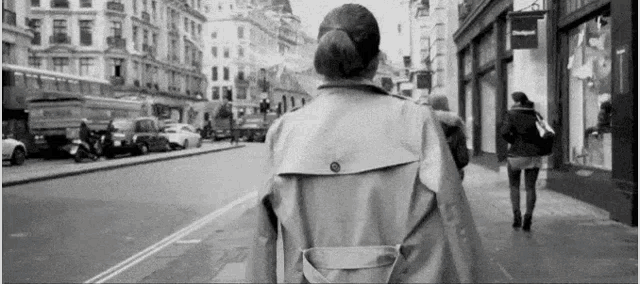 a woman in a trench coat is walking down a street
