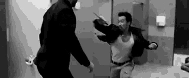 a man in a suit is fighting another man in a bathroom .