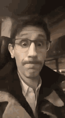 a man with glasses and a mustache is making a funny face in a car .