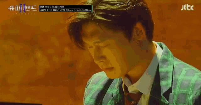 a man in a green suit is sitting in front of a screen that says jtbc on it