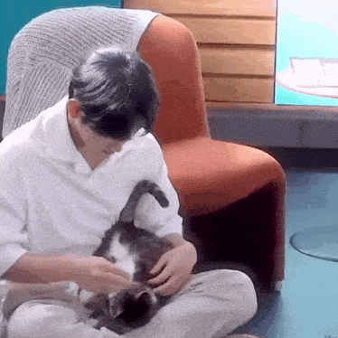 a man is petting a cat while sitting on the floor .