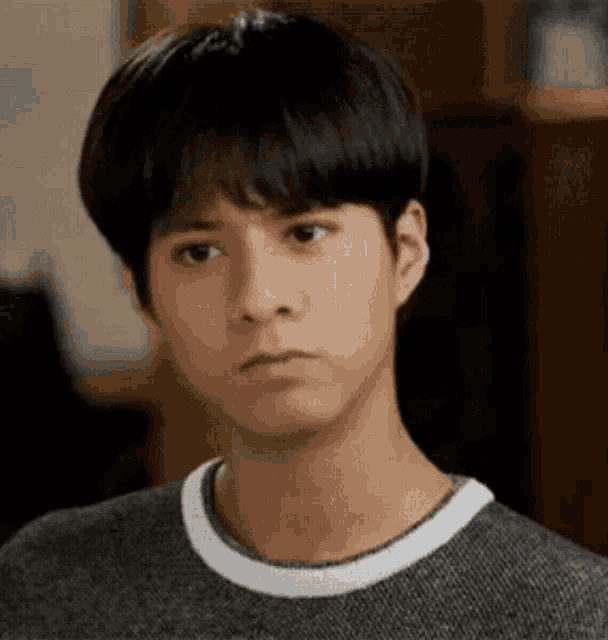 a young man wearing a grey sweater and a white collar is making a sad face .