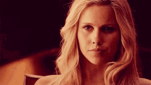 a woman with long blonde hair is sitting in a chair and looking at the camera with a serious look on her face .