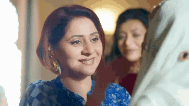 a woman in a blue shirt is smiling and looking at the camera .