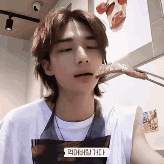 a young man is eating a piece of meat with chopsticks while wearing an apron .
