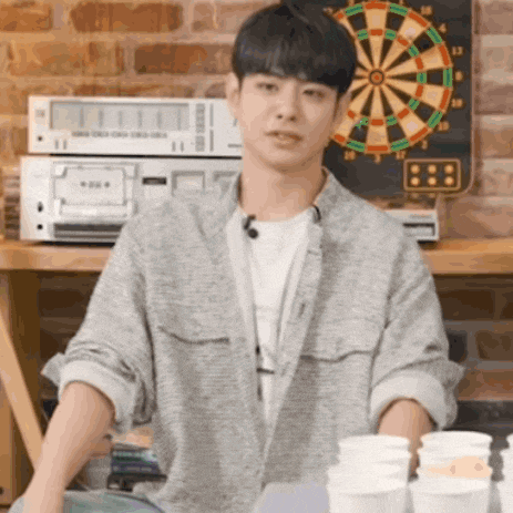a man is standing in front of a dart board and a stack of cups .