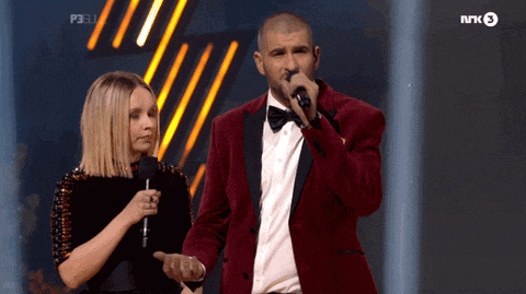 a man in a red suit is singing into a microphone while standing next to a woman