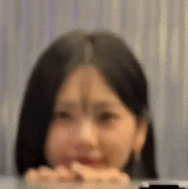 a blurry picture of a woman sitting at a table with her hand on her chin .
