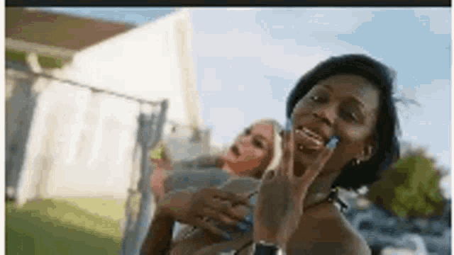 two women are standing next to each other in front of a fence . one of the women is wearing a bikini top .
