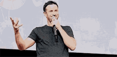 a man is holding a microphone in his hand and smiling while standing in front of a screen .