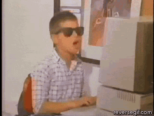 a man wearing sunglasses is sitting in front of a computer monitor ..