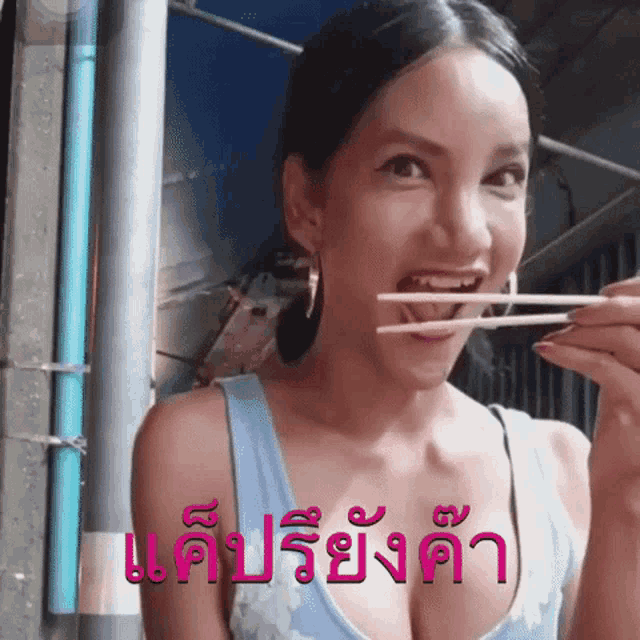 a woman in a blue tank top is holding chopsticks in her mouth with a foreign language written on the bottom right