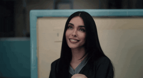 a woman with long black hair is smiling in front of a blue wall with the number 1 on it