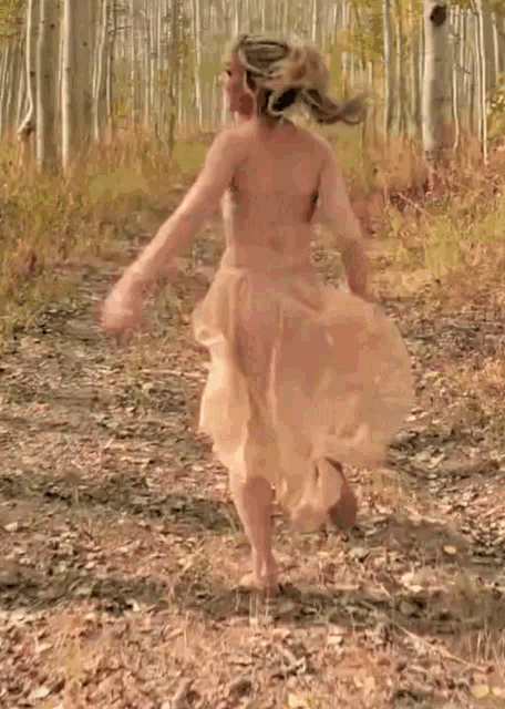 a woman in a long white dress is dancing in the woods