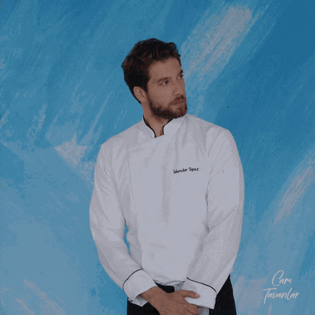 a man wearing a white chef 's jacket with a name embroidered on it is standing in front of a blue wall