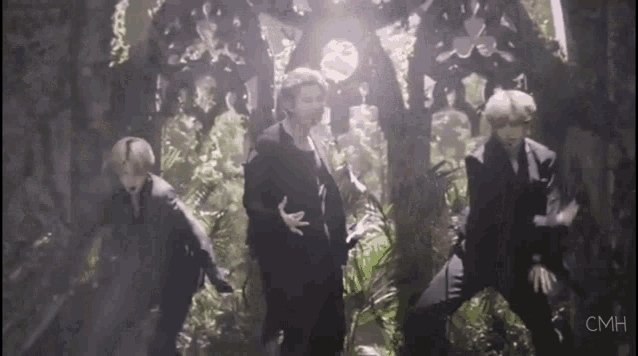 a group of men in suits are dancing in a dark room surrounded by plants .