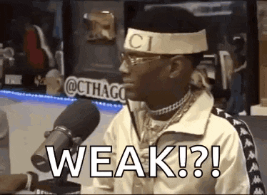 a man wearing a headband and glasses is sitting in front of a microphone and saying `` weak ? '' .