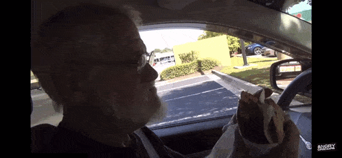 a man eating a sandwich in a car with the word angry written on the bottom