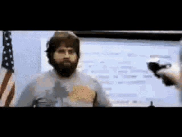 a man with a beard is talking into a microphone in front of an american flag ..