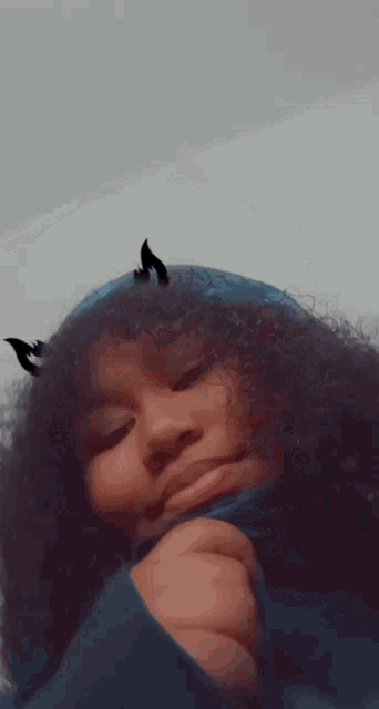 a young girl with curly hair and horns on her head is wearing a blue hoodie .
