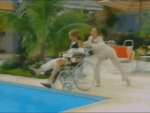 a woman in a wheelchair is being pushed into a swimming pool by another woman .