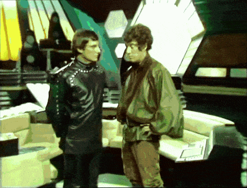 two men are standing next to each other in a room and one of them has a green jacket